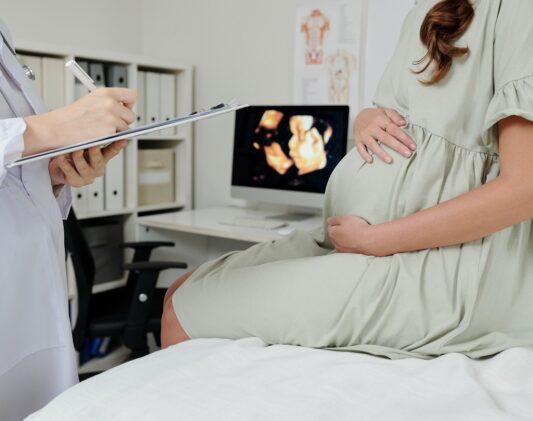 Close-up of doctor making notes in medical card after ultrasound exam of pregnant woman at hospital